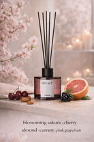 Diffuser with cherry, almond, currant, and pink grapefruit scents on a decorative surface with flowers and fruit.